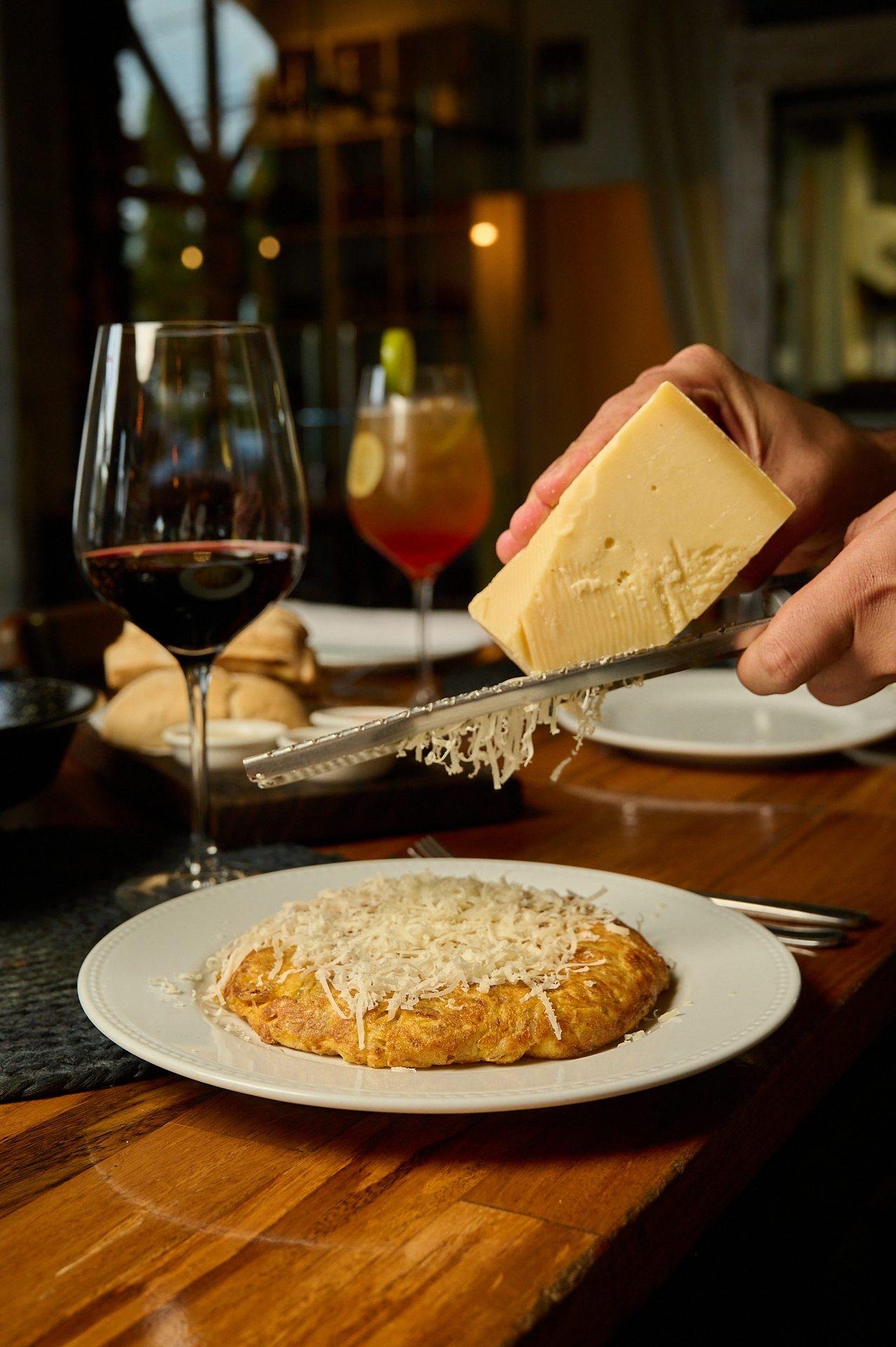 Queso rallado a la mesa sobre la tortilla española, servicio en sala